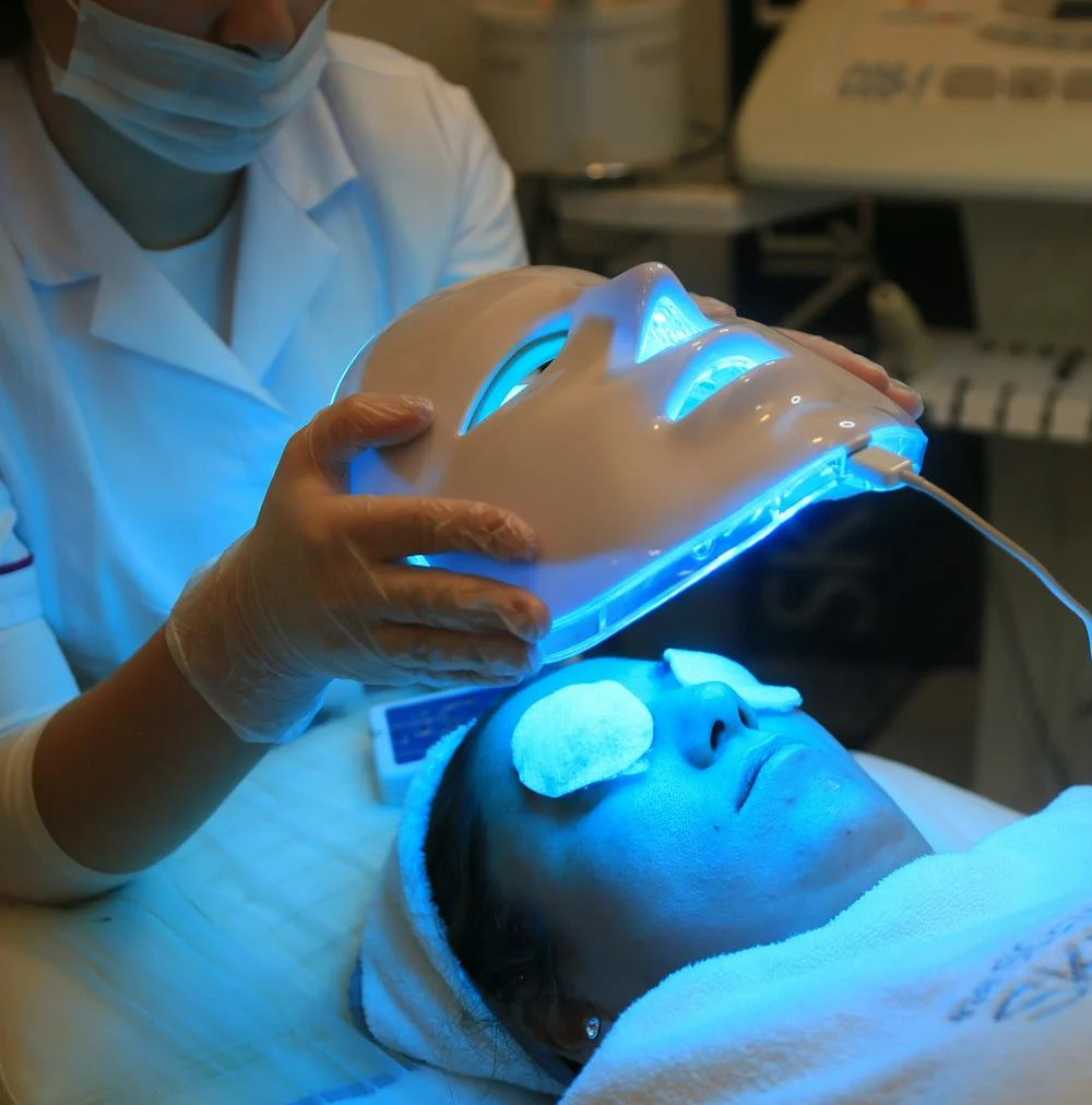 Aesthetician applying blue LED light therapy mask to a patient's face, highlighting the use of AI-powered skincare technology for personalized skin treatments