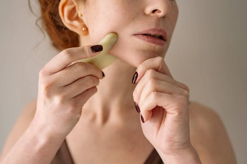 Close-up of a woman using a gua sha tool on her jawline for lymphatic drainage and skincare enhancement