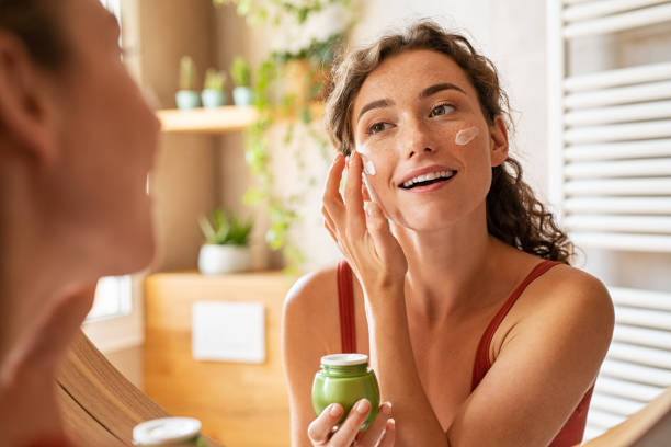 Smiling woman applying moisturizer to her face as part of her skincare routine.