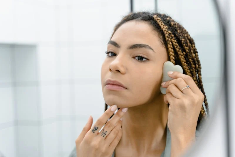 Woman using a Gua Sha tool on her face for lymphatic drainage massage, focusing on jawline and cheek area to reduce puffiness and improve circulation