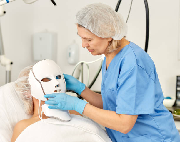 A professional esthetician applying an LED mask to a patient's face, representing advanced AI-powered skincare technology used for personalized skin treatments.