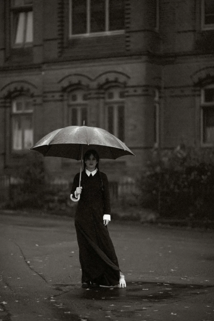 Person dressed in a gothic-inspired black outfit with an umbrella, capturing the dark and moody aesthetic popularized by Wednesday